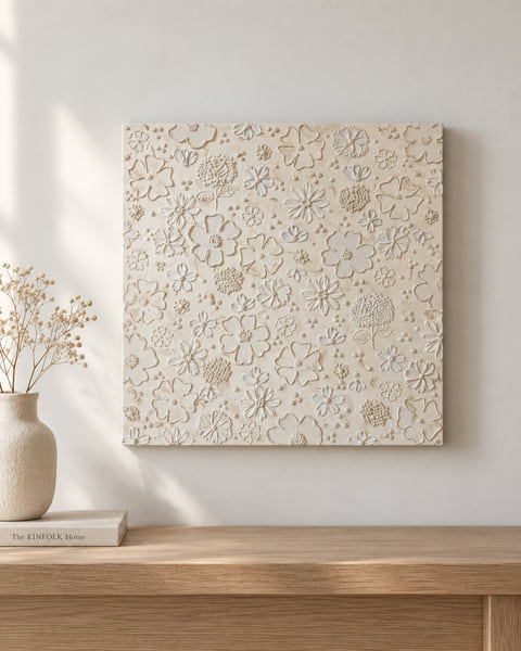 Square cream canvas densely covered in sculpted flowers with textured centres, hung above an oak sideboard