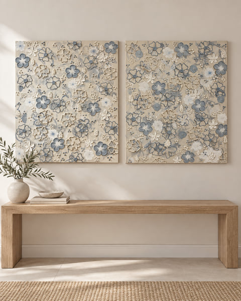 Two portrait canvases of sculpted blue and tan flowers, hung side by side above an oak bench
